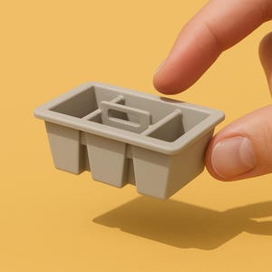 Puede incluir: Una bandeja de plástico gris con cuatro compartimentos y un asa. La bandeja está diseñada para contener objetos pequeños, como utensilios o artículos de oficina.