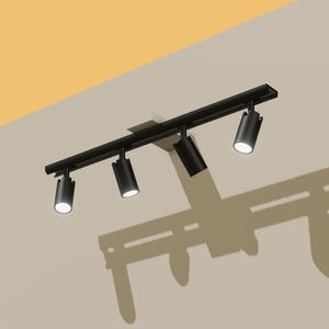 May include: A black track lighting fixture with four adjustable spotlights. The lights are mounted on a rectangular track and are angled downward. The fixture is mounted on a beige wall, casting a shadow.