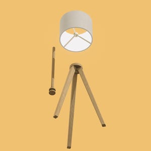 May include: A wooden tripod floor lamp with a white fabric lampshade. The lamp is disassembled, showing the separate parts.