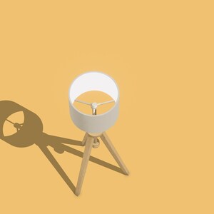 May include: A white lampshade with a wooden tripod stand casts a shadow on a yellow surface.
