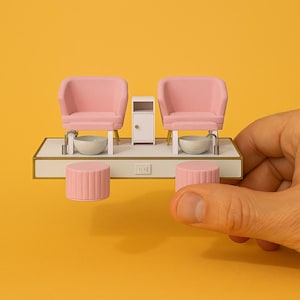 May include: A miniature pink pedicure station with two chairs, a small white cabinet, and two foot basins. The station is on a white platform with a gold trim. There are two pink footrests.