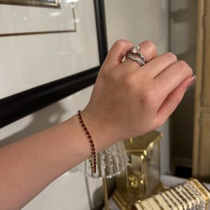 May include: A red gemstone bracelet with a delicate chain. The bracelet is on a person's wrist, and there is a ring on the same hand.