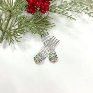 May include: Two silver-toned metal hair combs featuring wavy teeth and decorative circular tops encrusted with small, multicolored rhinestones in shades of pink, blue, green, and clear, arranged in a cluster pattern on each hair accessory.