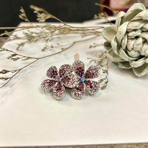 May include: Two silver flower hair clips with pink and iridescent rhinestones.