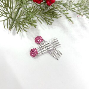 May include: A pair of silver-toned hair combs featuring rounded ends encrusted with small, vibrant pink crystals. The combs have wavy, multi-pronged teeth designed for securing hair, with the pink crystal embellishments positioned at the top.