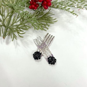 May include: Two silver-toned hair combs featuring a wavy metal design. Each comb is topped with a spherical cluster of small, faceted black beads that create a textured, dark appearance. The combs are positioned in a crossed arrangement.