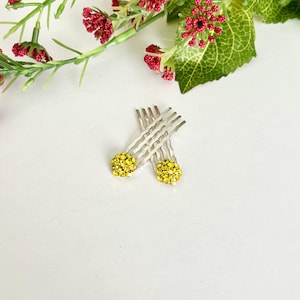 May include: Two silver-toned hair pins featuring circular decorative tops encrusted with small, bright yellow rhinestones. The pins have wavy metal prongs designed for securing hair, and the yellow stones create a textured, sparkling appearance.