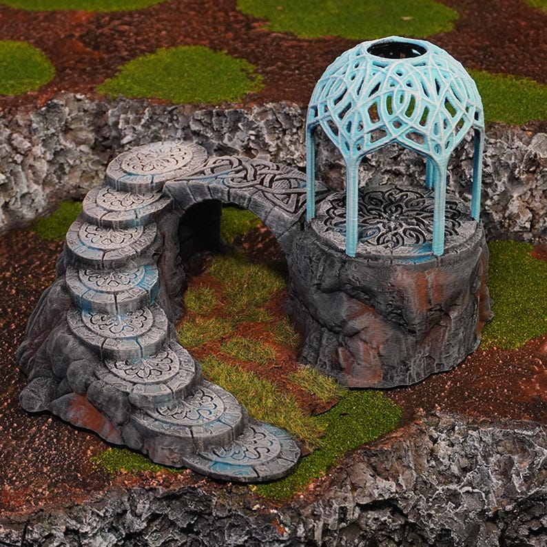 Pu&ograve; includere: Una scala di pietra in miniatura conduce a un arco in pietra, che collega a una piattaforma in pietra con un gazebo a cupola blu e intricato in cima.