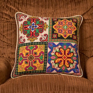 May include: Square decorative pillow with a white border. The pillow features a patchwork design with four distinct sections. Each section showcases a different geometric pattern in vibrant colors like red, green, yellow, and blue, creating a visually rich textile.
