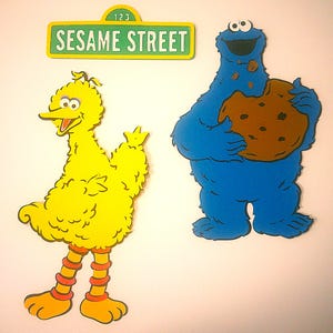 May include: Sesame Street-themed decorations featuring Big Bird, Cookie Monster holding a cookie, and a sign with the words "Sesame Street". The sign is green and yellow, and the characters are yellow and blue.