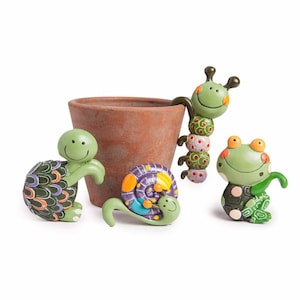 Puede incluir: Una maceta de terracota rodeada de cuatro adornos de jardín caprichosos. Los adornos incluyen una tortuga verde, un caracol morado y amarillo, una oruga verde y una rana verde. Los adornos son de colores brillantes y tienen caras sonrientes.