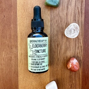 May include: A dark brown glass bottle with a dropper top, labeled "@HERBAL THERAPY.VA ELDERBERRY TINCTURE". The label also includes the ingredients, "ETHICALLY SOURCED ORGANIC ELDERBERRY (CONTAINS ALCOHOL)", and instructions to "SHAKE BEFORE USE" and "TO EVAPORATE ALCOHOL, ADD TINCTURE TO HOT WATER".