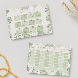May include: A 2027 calendar and a weekly planner featuring a botanical theme with light green monstera and palm leaf illustrations. The calendar displays twelve months, while the weekly planner includes columns for each day of the week.
