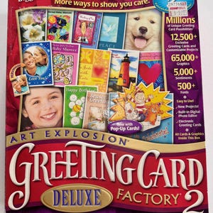 May include: A boxed set of the "Greeting Card Factory Deluxe 2" software. The box is red, purple, and gold, with images of greeting cards and a smiling dog. Text includes "Art Explosion" and "Millions of Unique Greeting Card Possibilities."