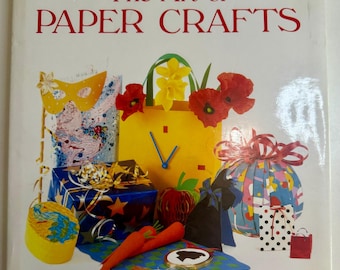 May include: A book cover titled "The Art of Paper Crafts" with colorful paper art illustrations. The cover features a yellow clock, gift boxes, flowers, and other paper craft creations. The author's name, Cheryl Owen, is at the bottom.