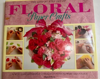 May include: A book titled "The Step by Step Art of Floral Paper Crafts" with a pink cover. The cover features a large floral arrangement made of paper flowers in shades of red and pink. The book also shows step-by-step instructions.