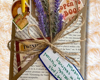 May include: A wrapped book with a sprig of purple lavender, a yellow pen, and stickers. The book is tied with twine and has a tag that reads "Mormon Historical Fiction, 19th Century, 447 pgs."