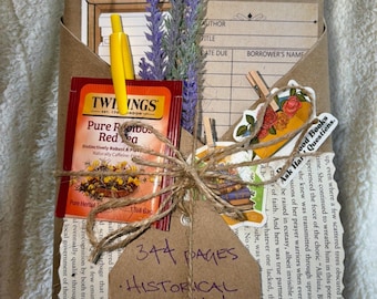 May include: A wrapped book with a tea bag, pen, and dried flowers. The book is tied with twine and has a tag with the text "344 PAGES, HISTORICAL CHRISTIAN FICTION, AMISH ROMANCE, 1970s, VIETNAM WAR."