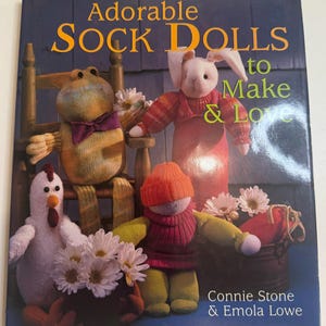 May include: A book cover titled "Adorable Sock Dolls to Make & Love" featuring handmade sock dolls. The dolls include a frog, a bunny, a chicken, and a doll wearing a hat. The cover also includes the authors' names, Connie Stone & Emola Lowe.