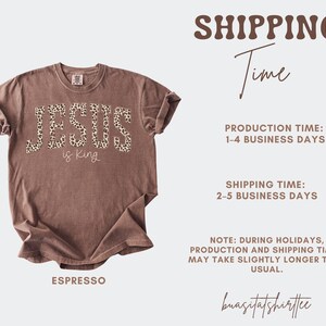 Op de afbeelding: Espresso-kleurig t-shirt met de tekst "JESUS is King" in een luipaardprint. Het shirt heeft een ronde hals en korte mouwen. De merknaam "buasitatshirttee" staat onderaan.