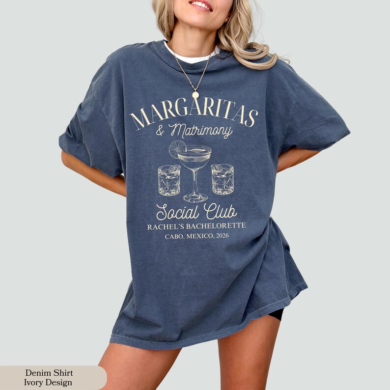 Może przedstawiać: Niebieska koszulka dżinsowa z kremowym napisem "MARGARITAS & Matrimony Social Club". Projekt zawiera szklanki do margarity i napis "RACHEL'S BACHELORETTE CABO, MEXICO, 2026". Koszulka ma luźny kr&oacute;j.