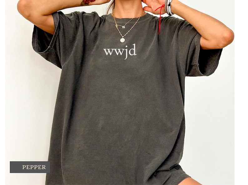 Puede incluir: Camiseta de gran tama&ntilde;o color pimienta con el texto "wwjd" en blanco. La camiseta tiene mangas cortas y un ajuste relajado. La tela parece suave y c&oacute;moda, adecuada para uso casual.