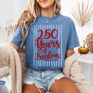 Woman wearing blue jean Comfort Colors patriotic shirt featuring “250 Years of Freedom Vintage 1776” retro red and blue design for Fourth of July celebration