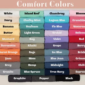 May include: A selection of folded t-shirts in a variety of colours, including white, pink, blue, and green. Each shirt is labelled with its colour name, such as "White," "Blossom," and "Chambray." The image displays a wide range of hues, from light pastels to deep, rich tones.
