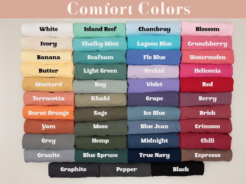 May include: A selection of folded t-shirts in a variety of colours, including white, pink, blue, and green. Each shirt is labelled with its colour name, such as "White," "Blossom," and "Chambray." The image displays a wide range of hues, from light pastels to deep, rich tones.