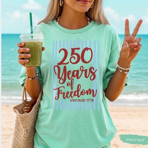 Woman wearing island reef Comfort Colors patriotic shirt featuring “250 Years of Freedom Vintage 1776” retro red and blue design for Fourth of July celebration
