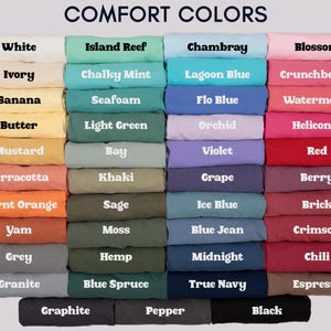 May include: A color chart displaying a variety of fabric colors, including white, ivory, and black. The text "COMFORT COLORS" is at the top. Each color is labeled with its name, such as "Island Reef," "Chambray," and "Blossom."
