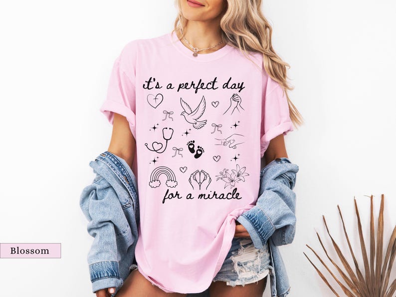 May include: Pink t-shirt with the text "it's a perfect day for a miracle" and various small black and white illustrations including a dove, a rainbow, a stethoscope, a heart, and footprints.