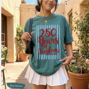 Woman wearing blue spruce Comfort Colors patriotic shirt featuring “250 Years of Freedom Vintage 1776” retro red and blue design for Fourth of July celebration