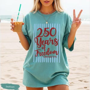 Woman wearing seafoam Comfort Colors patriotic shirt featuring “250 Years of Freedom Vintage 1776” retro red and blue design for Fourth of July celebration