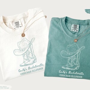 May include: Two t-shirts, one ivory and one light green, each with a cowboy hat and boot design. The text "Emily's Bachelorette CHICAGO ILLINOIS" is printed below the graphic. Each shirt has a gold necklace.