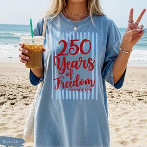 Woman wearing blue jean Comfort Colors patriotic shirt featuring “250 Years of Freedom Vintage 1776” retro red and blue design for Fourth of July celebration