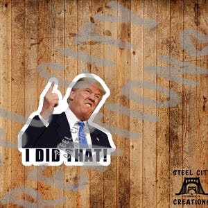 May include: A white sticker with a photo of a man in a suit pointing his finger up and the text "I DID THAT!" printed in black. The sticker has a white border and is on a wood background.