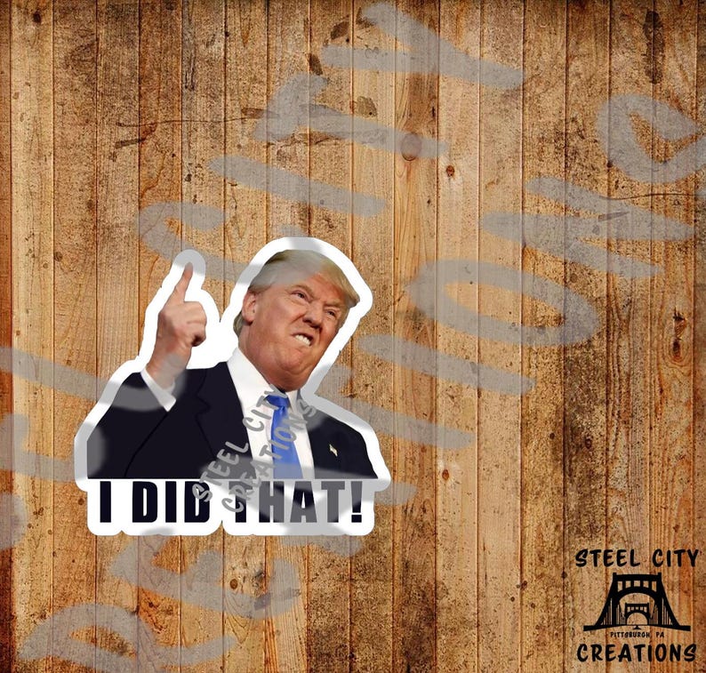 May include: A white sticker featuring a photograph of a man in a suit pointing upwards, with the text "I DID THAT!" printed in black. The sticker has a white border and is displayed against a wooden backdrop.