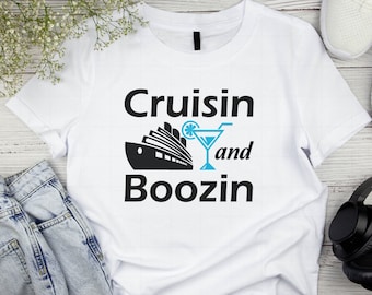 May include: White t-shirt with black text that reads "Cruisin and Boozin". A black silhouette of a cruise ship and a blue cocktail glass with a lime wedge are above the text.