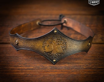 May include: A brown leather headband with a tree of life design embossed in the center. The headband is decorated with brass studs and has a black leather strap for adjusting the fit.