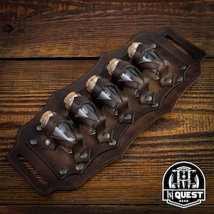 May include: A brown leather belt with five small glass vials with cork stoppers. The belt has metal rivets and is designed to hold the vials securely. The belt is on a wooden surface.