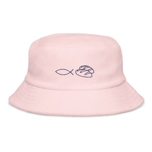 May include: A pink bucket hat with a blue embroidered design of a fish and two loaves of bread.