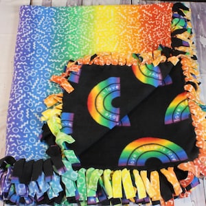 May include: A colorful fleece blanket featuring a rainbow gradient design and a black section with rainbow arches and the words "love is love." The blanket has a fringed edge in various rainbow colors. The blanket is a cozy and vibrant home decor item.