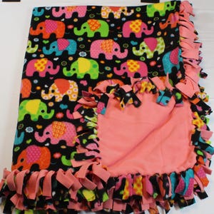May include: A pink and black fleece tie blanket with a colorful elephant print. The blanket has a fringe border and is made of soft, cuddly fabric.