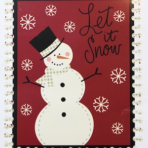 May include: A festive card featuring a snowman with a black top hat, scarf, and twig arms, set against a red background with snowflakes and the words "Let it Snow." The card has a decorative border.