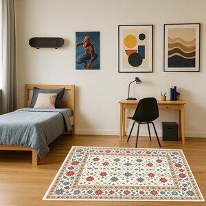 Pode incluir: Tapete retangular creme com um padrão floral detalhado em vermelho, azul-petróleo e dourado. O tapete está colocado sobre um piso de madeira em um quarto com uma cama, uma mesa e obras de arte.