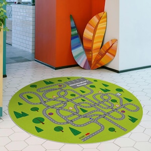 Könnte beinhalten: Ein runder, grüner Spielteppich mit einem Straßenkarten-Design. Der Teppich hat graue Straßen, grüne Bäume und Verkehrsschilder. Der Text "Christopher's Garage" ist auf dem Teppich aufgedruckt. Der Teppich hat einen Durchmesser von etwa 122 cm.
