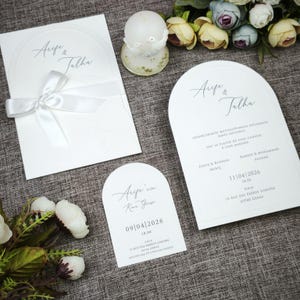 May include: A white ceramic mug with a black handle and the text "But First, Coffee" in a bold, black font. The mug is sitting on a wooden surface, and the background is blurred.