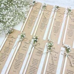 Może przedstawiać: Zestaw oł&oacute;wk&oacute;w z dołączonymi aranżacjami kwiatowymi i drukowanymi kartkami. Każdy oł&oacute;wek ozdobiony jest małym bukietem białych kwiat&oacute;w związanym sznurkiem. Kartki zawierają tekst oraz imiona "Hamdi & Jasmin" z datą "29.06.2024".