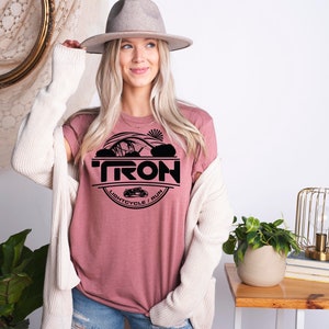 May include: A pink t-shirt with a black graphic design of a Tron lightcycle and the word "TRON" in a circle. The text below the lightcycle reads "Lightcycle / Run".